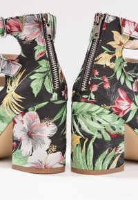 Sandales à talons blocs en tissu noir affichant des motifs floraux tropicaux multicolores et des fermetures éclair à l'arrière.