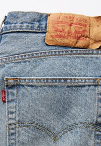 Vaqueros de mezclilla de color azul desgastado, con una etiqueta de cuero cosida en la cintura y una etiqueta roja de Levi's en el bolsillo trasero.