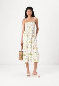 Φλορικό φόρεμα με κα smocked κορσέ, λεπτές τιράντες και ρέουσα φούστα. Λευκό φόντο με πράσινες, κίτρινες και κόκκινες λεπτομέρειες.