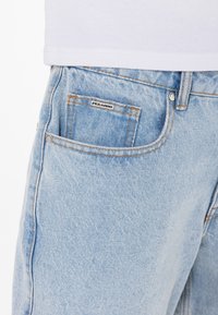 Světle modré džíny z denimu s klasickým pětipocketovým designem, viditelným švem a značkovou nášivkou na přední kapse.