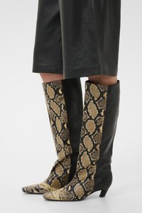 Μποτάκια μέχρι το γόνατο με μυτερές μύτες και χαμηλές τακούνια, με μαύρα δερμάτινα πάνελ και μπροστινό και πλευρικά μέρος με σχέδιο δέρματος φιδιού.