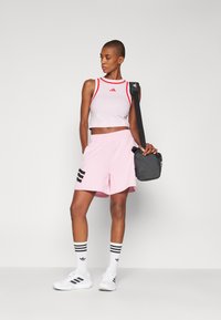 Lichtroze cropped tanktop met rode accenten, roze shorts met zwarte strepen, witte sneakers en een zwarte schoudertas.