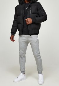 Czarna pikowana kurtka z kapturem obszytym futrem, dwie kieszenie na zamek. Połączona z jasnoszarymi spodniami dresowymi i białymi trampkami. Gładkie materiały.