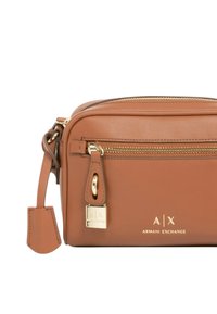 Borsa a tracolla in pelle marrone con hardware dorato, tasche con zip e logo impresso. Forma rettangolare compatta con una consistenza liscia.