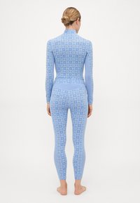 Mulher em pé, descalça, de costas, vestindo uma blusa de manga longa azul com um padrão e leggings combinando com um design de floco de neve.