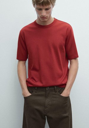 Red short-sleeve t-shirt made of cotton, featuring a crew neck and relaxed fit, paired with dark brown trousers.