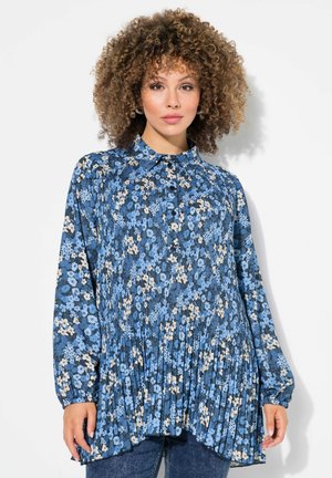Blauwe bloemenblouse met een geplooid ontwerp, met lange mouwen en een knopenrij aan de voorkant. De stof vertoont ingewikkelde patronen van lichte en donkere bloemen.