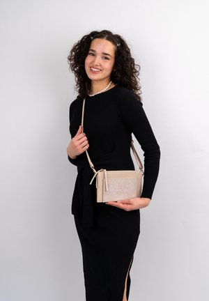 Borsa a tracolla beige con una parte anteriore texturizzata, lati lisci e hardware dorato. Tracolla regolabile e design minimalista, indossata in modo casual.