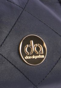 Bolso de piel azul marino con un diseño acolchado y una placa con el logo dorado redondo etiquetada "don algodon" exhibida de forma prominente.