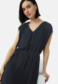 Dunkel plissiertes Kleid mit V-Ausschnitt und kurzen Ärmeln, ausgestattet mit einem Kordelzug in der Taille für eine verstellbare Passform. Glatter, strukturierten Stoff.