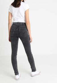 Jeans ajustados de denim negro desgastado, con una cintura alta, bolsillos traseros y un corte entallado, combinados con una camiseta blanca básica y zapatillas blancas.