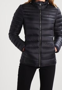 Svart puffjacka med blixtlås fram, hög krage, horisontellt quiltad design och sidofickor. Tillverkad av lätt, slätt material.