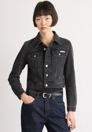 Black denim cropped jacket with button closure, two front pockets, and a slim fit design. Worn over dark blue jeans and a black belt.
