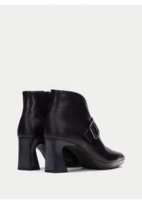 Par de botas de cuero negras por el tobillo con tacones cuadrados y detalle de hebilla lateral, mostradas desde ángulos trasero y lateral sobre un fondo blanco.