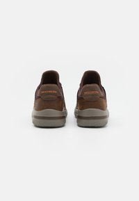Le scarpe Skechers brown presentano una tomaia in pelle liscia e tessuto testurizzato, un colletto imbottito e una suola in gomma con un battistrada decorato.