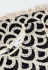 Černá a béžová háčkovaná látka s spirálovými vzory. Okraje mají třásně. Uprostřed je viditelný štítek.