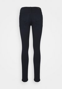 Jean skinny bleu foncé vu de dos avec deux poches arrière et passants de ceinture sur un fond blanc uni.