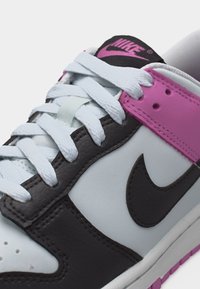 Κοντινή λήψη ενός λευκού, μαύρου και ροζ αθλητικού παπουτσιού Nike με λευκά κορδόνια και ροζ λογότυπο Nike στη γλώσσα.