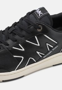 Scarpa da ginnastica nera con tomaia in pelle testurizzata, accenti bianchi a zigzag, sistema di allacciatura prominente e linguetta imbottita con logo.