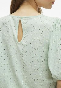 Blusa verde menta chiaro con un motivo testurizzato, maniche a palloncino corte e apertura a chiave sul retro per un tocco di dettaglio.