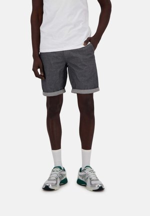Graue Jeansshorts mit umgeschlagenen Säumen, kombiniert mit einem weißen T-Shirt und silber-grünen Sportschuhen, die ein einfaches Design und einen lockeren Sitz aufweisen.