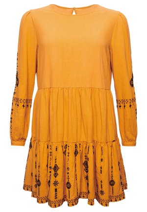 Langarmige, mosterdgele jurk met een geplooemde zoom en fijne zwarte borduursels langs de mouwen en onderkant. Detail met een keyhole aan de achterkant.