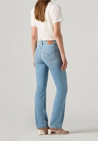 Vaaleansinisen denimin farkut liehuvilla lahkeilla, joissa on nahkainen merkki vyötäröllä ja ommellut takataskut. Yhdistetty valkoiseen t-paitaan.