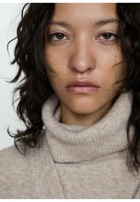 Bežový rolák vyrobený z mäkkého, textúrovaného pleteného materiálu. Tkanina má rebrovaný golier s drobnými variáciami farby a vláknami.