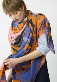 Ein mehrfariger Schal mit geometrischen Mustern in Orange, Blau, Pink und Grün, aus weichem Material mit fransigen Kanten.