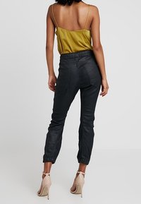 Svarta läderjoggingbyxor med elastisk midja, smal passform och avsmalnande anklar; matchat med en senapsgul silkjumpsuit.