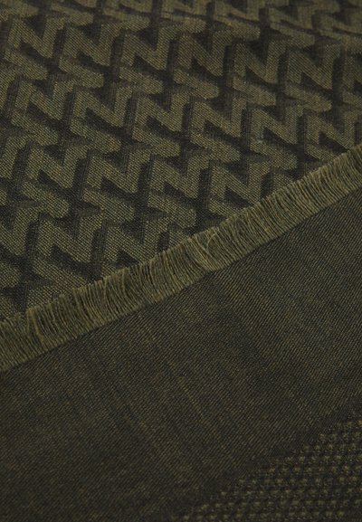 Woven scarf in dark green featuring a repeated zigzag pattern, frayed edges, and a textured finish. Material appears soft and lightweight.