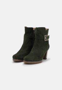 Zelené semišové kotníkové boty s bočním zipem, akcentem s přezkou a cylindrickým podpatkem. Mají hladký povrch a zaoblený design špičky.