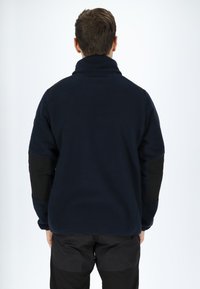 Pullover in fleece navy con colletto alto, superficie texturizzata e toppe nere sui gomiti. Orlo regolabile, vestibilità rilassata, senza marchio visibile.