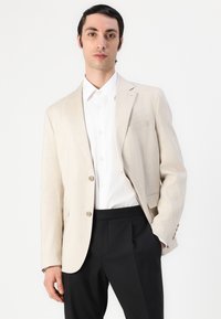 Beige linblazer med to knapper, enkelt lomme på venstre side, kombinert med en hvit skjorte og sorte bukser. Glatt tekstur, skreddersydd passform.