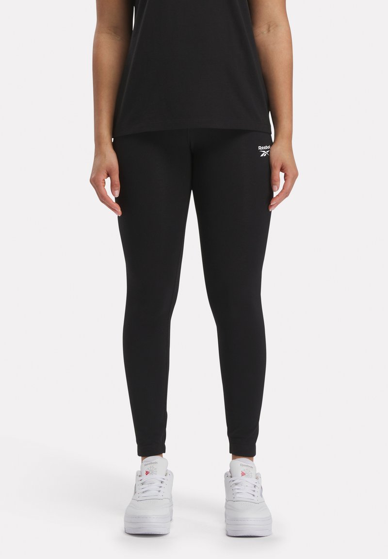 Crne tajice izrađene od rastezljivog materijala, s uskim krojem i malim bijelim Reebok logom na lijevom kuku. Nosene s bijelim tenisicama.