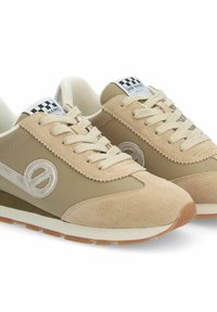 Beige sneakers met een combinatie van suède en stoffen bovenzijde, voorzien van een zilveren logo aan de zijkant, witte veters en een bruine rubberen zool.