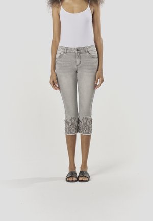 Graue Denim-Caprihosen mit floralem Stickmuster am Saum, schmaler Schnitt, leicht ausgefranste Kanten, kombiniert mit schwarzen Sandalen.
