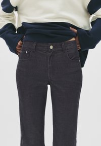 Jeans din denim închis, cu o croială slim, design cu cinci buzunare și un nasture frontal argintiu. Material texturat cu linii verticale subtile.