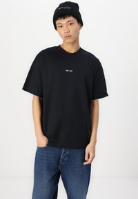 Svart bomull T-skjorte med korte ermer, med en liten hvit "CORE DEPT." logo på brystet. Kombinert med blå denim jeans.