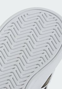 Bijeli potplat tenisice s teksturiranim cik-cak uzorkom; ima glatki rub i svijetlosivu gornjište s blagim sjajem.