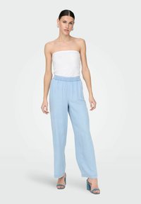 Pantalons larges bleu clair en tissu doux, avec une taille élastique. Assortis à un haut sans manches blanc et des talons bleus.