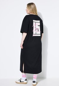 Czarna sukienka t-shirtowa z krótkimi rękawami, bocznymi rozcięciami i grafiką „Love” w kolorze białym i różowym na plecach. Połączona z skarpetami w wielokolorowe paski i trampkami.