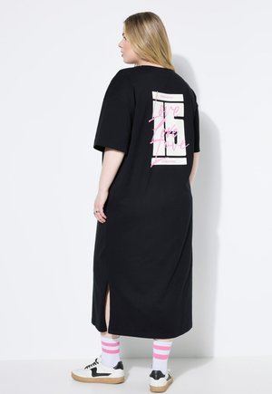 Abito t-shirt nero con maniche corte, fessure laterali e una grafica bianca e rosa con la scritta "Love" sulla schiena. Abbinato a calzini a righe multicolori e sneakers.