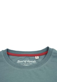 Teal bomulds T-shirt med rund halsudskæring, kontrasterende rød indvendig kant og hvidt logo-tekst på kraven. Størrelsesmærket viser 98/104.