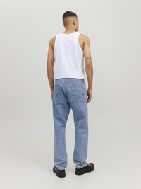 Jean en denim bleu clair à coupe décontractée, associé à un débardeur blanc sans manches. Comprend des poches arrière et un patch en cuir avec logo.