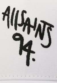 Cappello bianco con un audace testo ricamato in nero che recita "AllSaints 94". Il materiale sembra liscio con una forma strutturata e dettagli cuciti.
