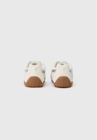 Scarpe da ginnastica bianche con accenti grigi e suole in gomma marrone. Presentano un materiale superiore liscio e una suola texture per una migliore aderenza.