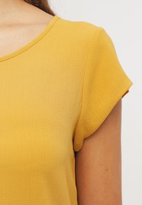 T-shirt à manches courtes et col rond en tissu texturé jaune moutarde, avec un léger éclat et une coupe décontractée.