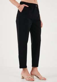 Pantalons noirs taille haute avec une ceinture élastique, poches latérales et une conception de jambe fuselée. Texture lisse avec des ourlets roulés aux chevilles.