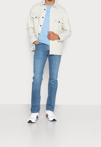 Ljusgrå skjorta med knappar och två bröstfickor, ljusblå t-shirt, blå jeans och vita sneakers med marinblå och röda detaljer.